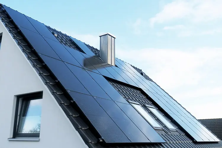 Photovoltaikanlage mit schwarzen Modulen auf einem Ziegeldach vor blauem Himmel