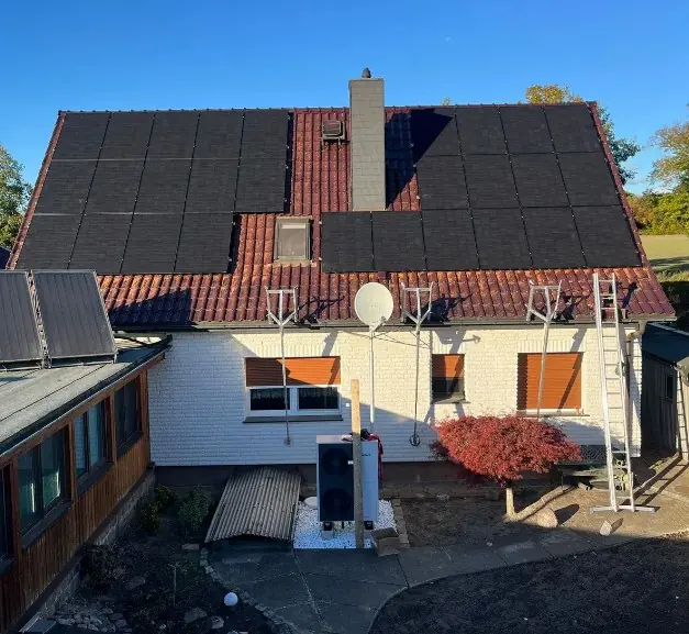 Wohnhaus mit Wärmepumpen-Außengerät, Photovoltaik und Solarthermie auf dem Dach